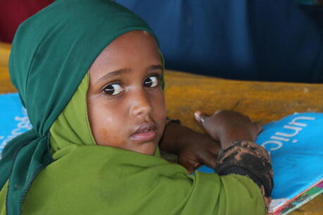In Somalia, a young girl sits at a desk with her workbook and pencil at a UNICEF-supported temporary learning center for children displaced by severe drought. 