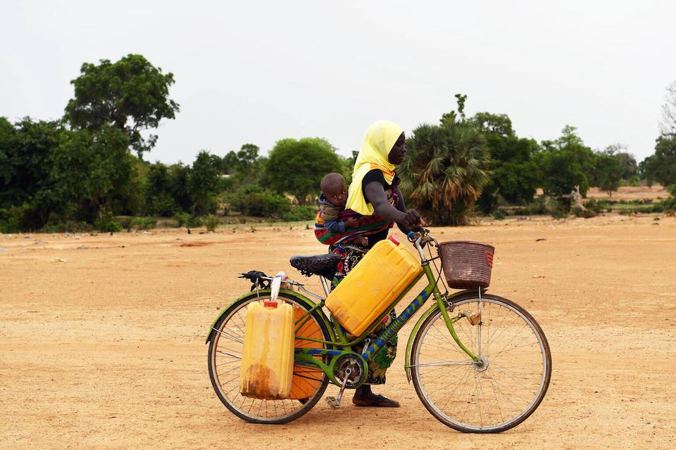 With her child on her back, a mother travels by bicycle to collect water from a well in Fada N'Gourma, Burkina Faso.