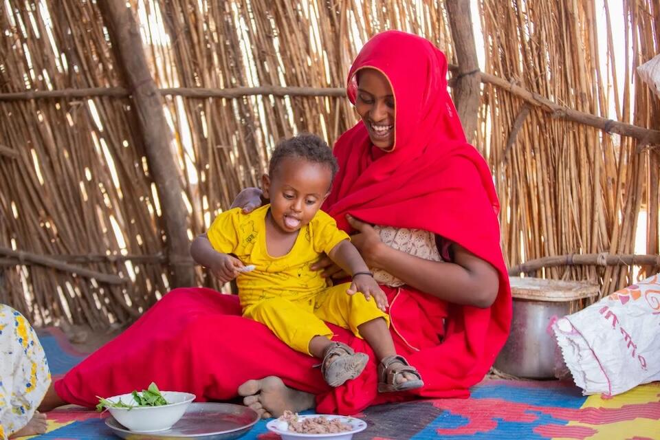 Ohag, a mother in Kassala state, feeds her child a balanced meal that includes leafy green vegetables she grew herself in a garden she planted with support from UNICEF.