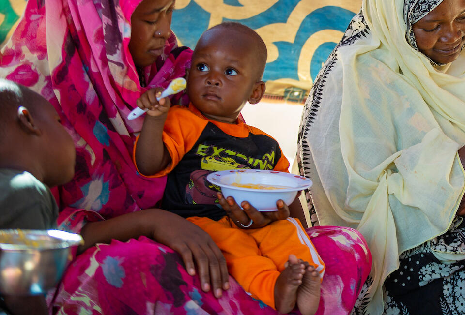 Using a complementary bowl and spoon, a mother in Kassala state, Sudan, feeds her child during a demonstration related to child nutrition led by a UNICEF-trained member of a Mother Support Group.