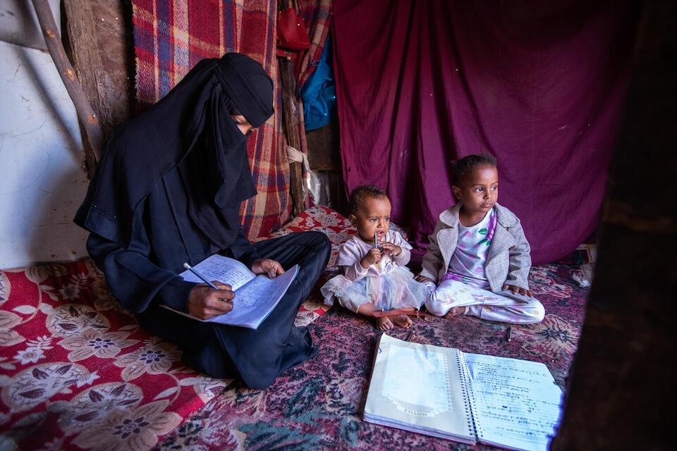 Yousra, 16,does homework for her UNICEF-supported literacy and numeracy classes with her young daughters by her side in Taizz, Yemen. 